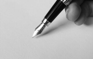 a black and white photo of a hand writing with a fountain pen